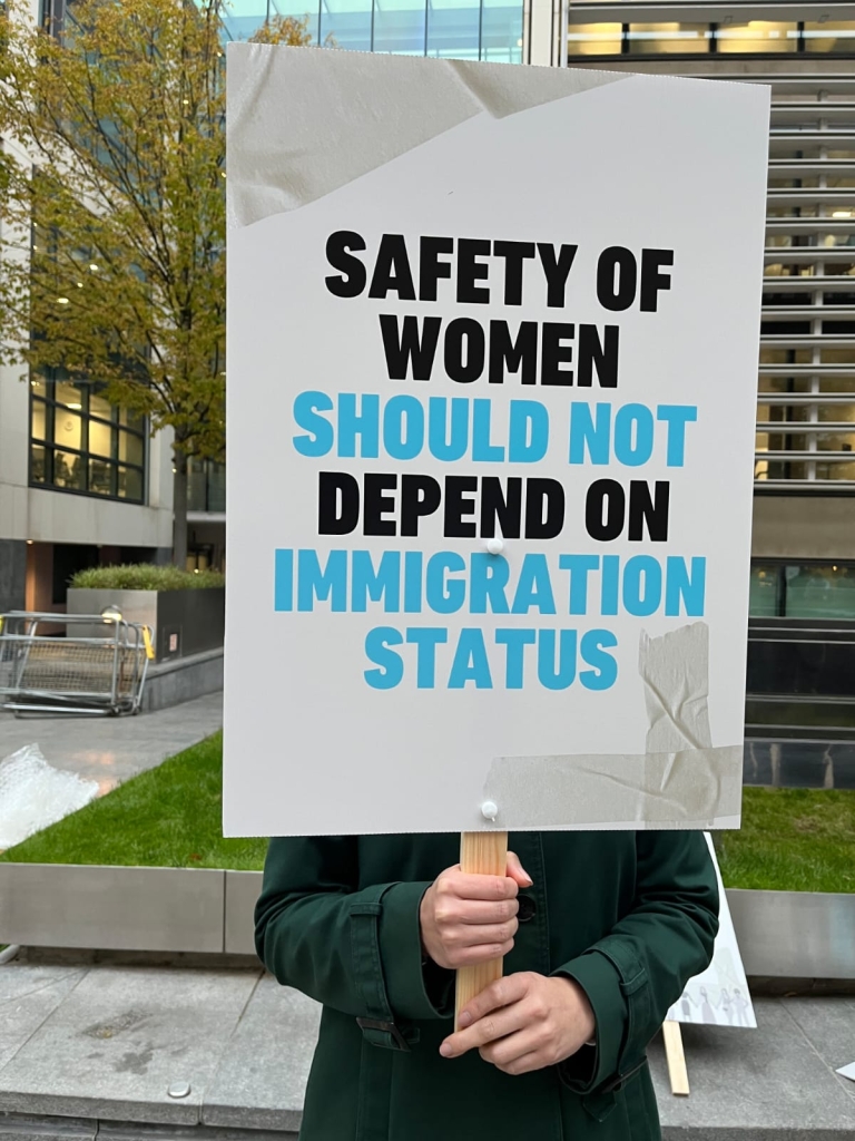 A placard reading “Safety of women should not depend on immigration status.”