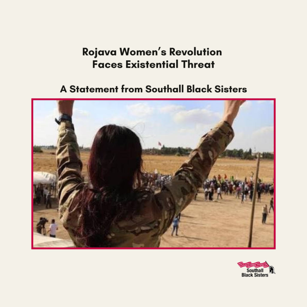 A woman in camouflage raises her arms before a crowd in a field, with text reading “Rojava Women’s Revolution Faces Existential Threat” and “A Statement from Southall Black Sisters.”